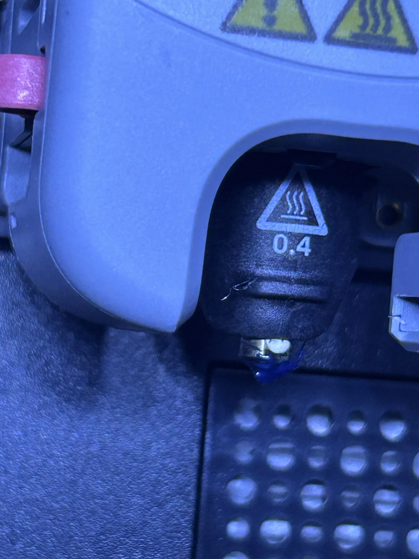A close-up of the installed 0.4 millimetre nozzle, with navy plastic visible near its tip under blue lighting.